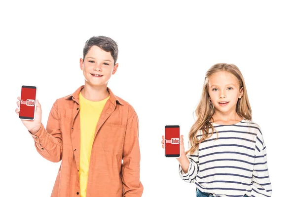 KYIV, UCRAINA - 9 SETTEMBRE 2019: vista frontale di due bambini sorridenti che tengono smartphone con app youtube su schermi isolati su bianco — Foto stock