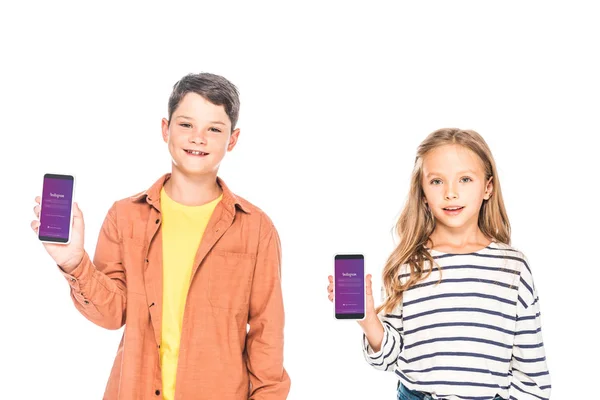 KYIV, UKRAINE - SEPTEMBER 9, 2019: front view of two smiling kids holding smartphones with instagram app on screens isolated on white — Stock Photo