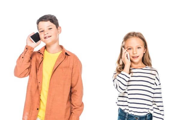 Два улыбающихся ребенка разговаривают на смартфонах изолированные на белом — стоковое фото
