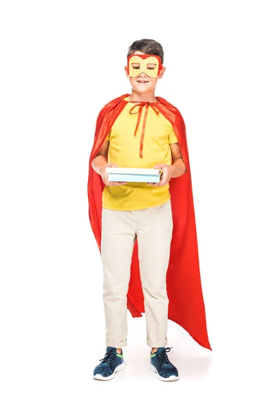 Full length view of kid in mask and hero cloak holding books on white — Stock Photo