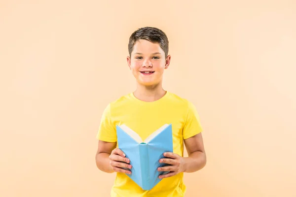 Вид спереди мальчика в желтой футболке, держащего в руках книгу, изолированную на розовом — стоковое фото