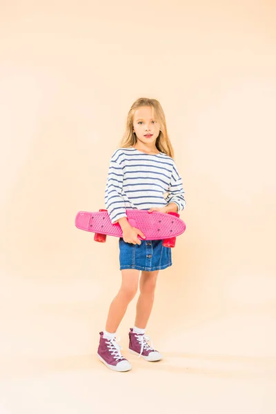 Full length view of kid in denim shirt holding skateboard on pink — Stock Photo