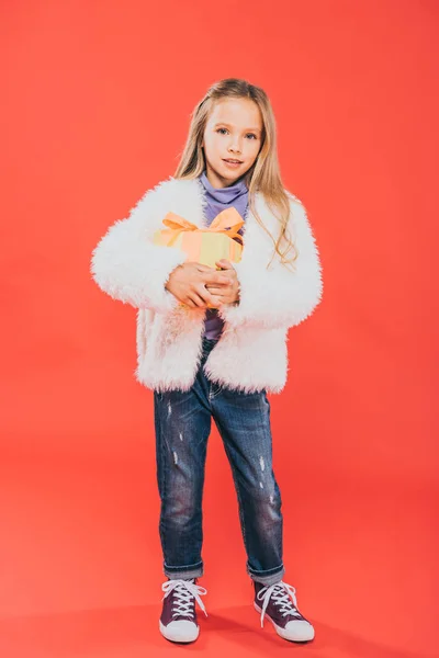 Full length view of kid holding gift box on red — Stock Photo