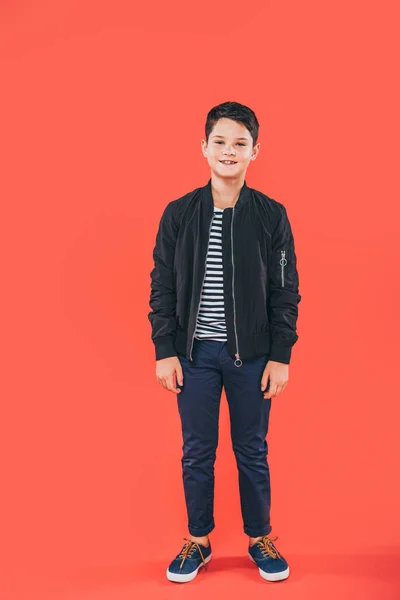 Full length view of smiling kid in jacket standing on red — Stock Photo