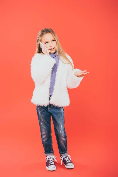 Full length view of kid in autumn outfit talking on smartphone on red — Stock Photo