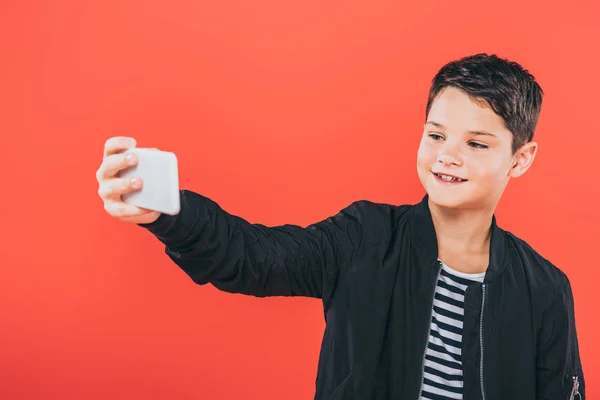 Niño sonriente en chaqueta tomando selfie aislado en rojo - foto de stock