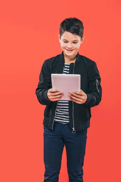 Lächelndes Kind in Jacke mit digitalem Tablet isoliert auf Rot — Stockfoto