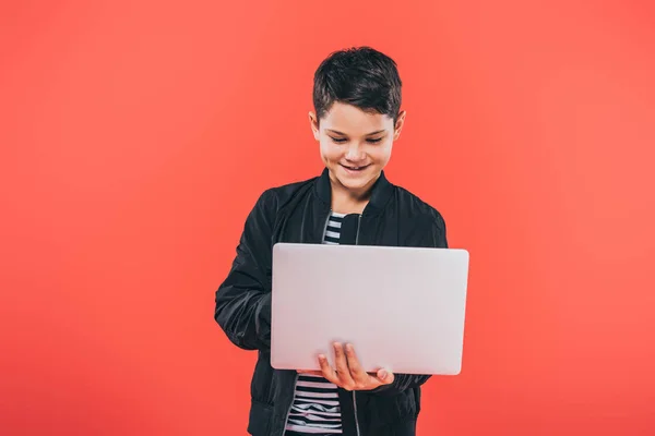 Vista frontale del bambino sorridente in giacca utilizzando laptop isolato su rosso — Foto stock