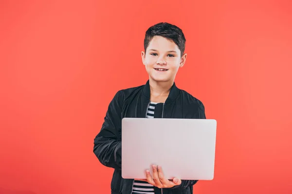 Vista frontale del bambino sorridente in giacca utilizzando laptop isolato su rosso — Foto stock