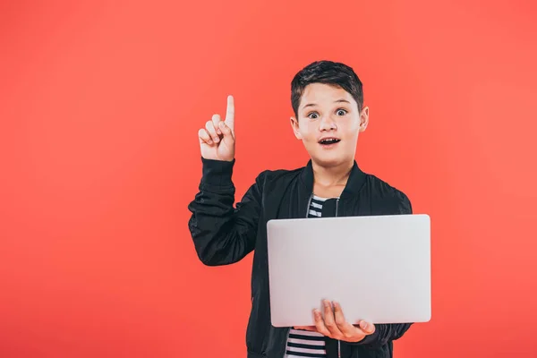 Front view of amazed kid in jacket using laptop and showing idea sign isolated on red — Stock Photo