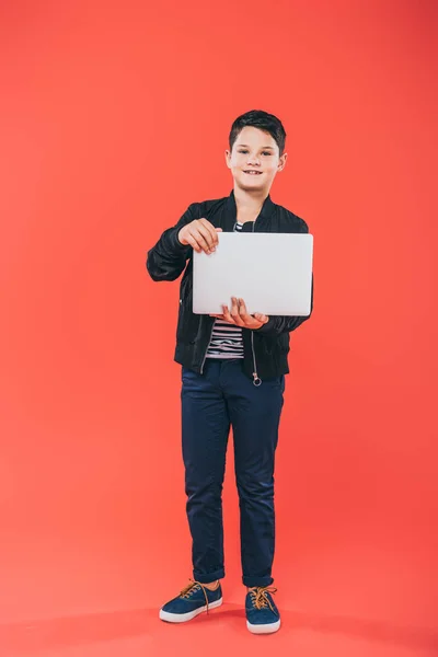 Full length view of smiling kid using laptop on red — Stock Photo