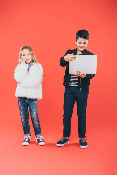 Ganzkörperansicht von Kindern mit Smartphone und Laptop auf rot — Stockfoto