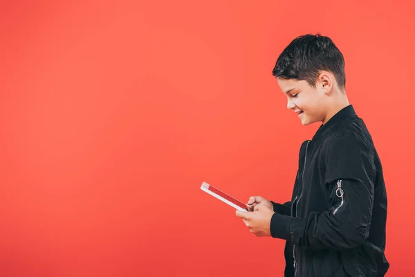 Visão lateral da criança sorridente usando comprimido digital isolado em vermelho — Fotografia de Stock