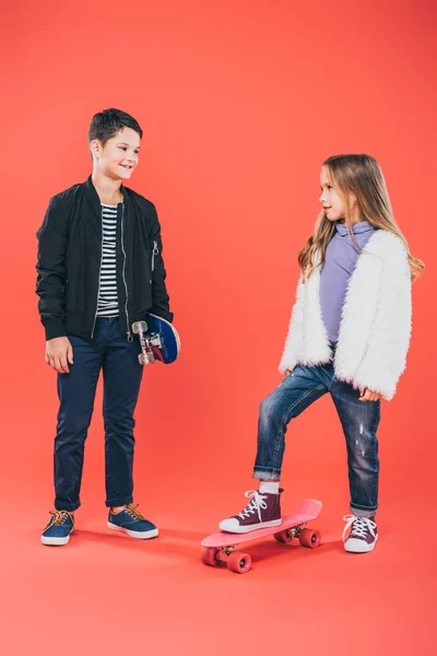 Visão de comprimento total de duas crianças com skates olhando um para o outro em vermelho — Fotografia de Stock