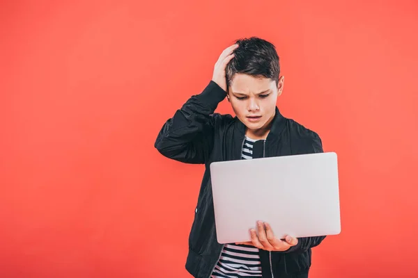 Vue de face de l'enfant confus en utilisant un ordinateur portable isolé sur rouge — Photo de stock