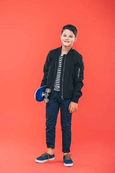 Vue pleine longueur de l'enfant souriant avec planche à roulettes sur rouge — Photo de stock