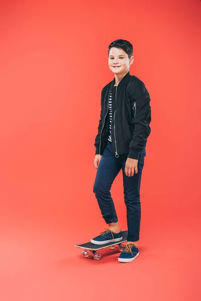 Vue pleine longueur de l'enfant souriant avec planche à roulettes sur rouge — Photo de stock