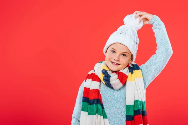 Vista frontal de niño sonriente en sombrero y bufanda aislado en rojo - foto de stock