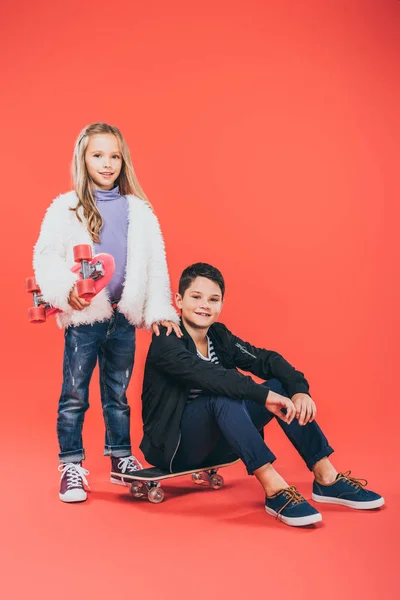 Дві усміхнені діти в осінньому вбранні зі скейтбордами на червоному — стокове фото