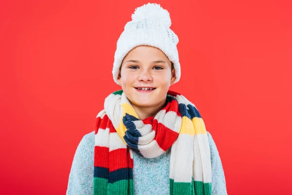 Vista frontal de niño sonriente en sombrero y bufanda aislado en rojo - foto de stock