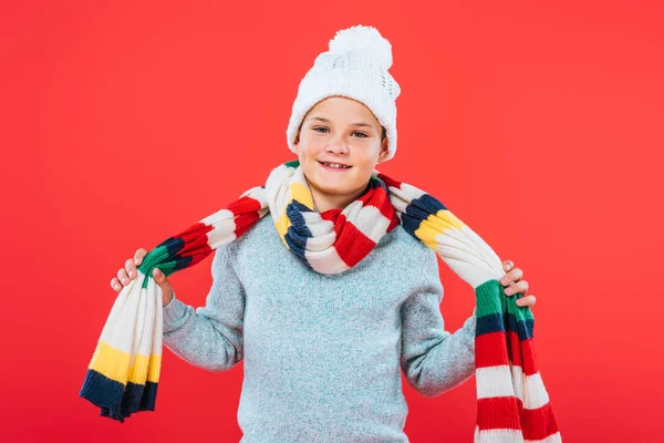 Vista frontal de niño sonriente en sombrero y bufanda aislado en rojo - foto de stock