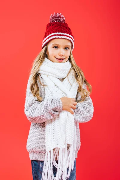 Enfant souriant dans le chapeau et l'écharpe isolé sur rouge — Photo de stock