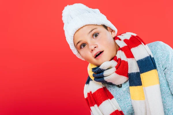 Niño sorprendido en sombrero y bufanda aislado en rojo - foto de stock