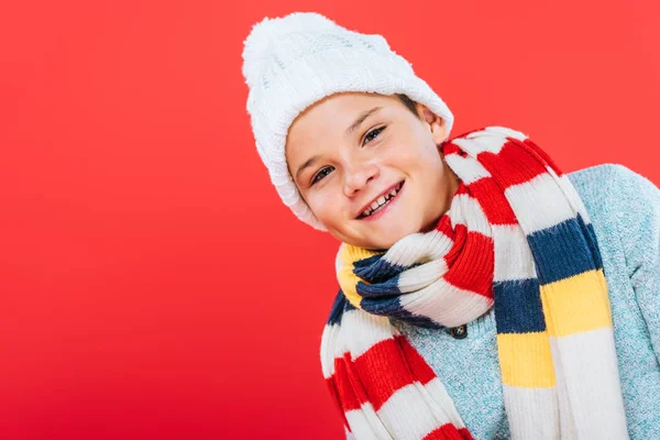 Niño sonriente en sombrero y bufanda aislado en rojo - foto de stock