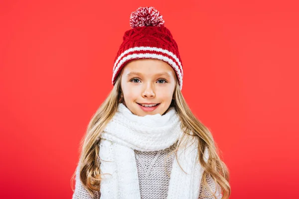 Vista frontal de niño sonriente en sombrero y bufanda aislado en rojo - foto de stock