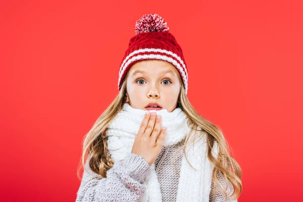 Visão frontal da criança chocada em chapéu e cachecol isolado no vermelho — Fotografia de Stock