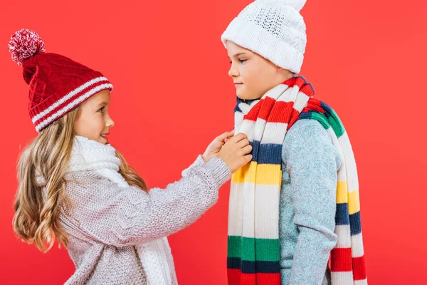 Dos niños en sombreros y bufandas mirándose aislados en rojo - foto de stock