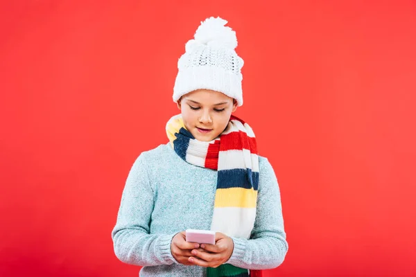 Vista frontal del niño en traje de invierno utilizando teléfono inteligente aislado en rojo - foto de stock