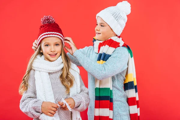 Duas crianças sorridentes em roupas de inverno isoladas no vermelho — Fotografia de Stock