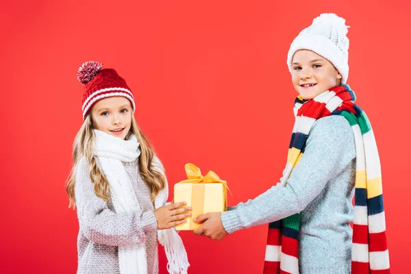 Dos niños sonrientes en trajes de invierno con presente aislado en rojo - foto de stock