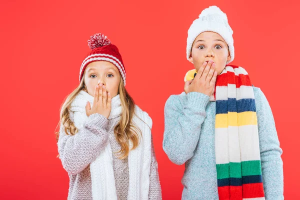 Vista frontal de dos niños sorprendidos en trajes de invierno aislados en rojo - foto de stock