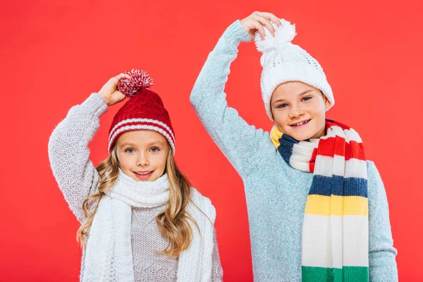 Два улыбающихся малыша в зимних нарядах, изолированных на красном — стоковое фото