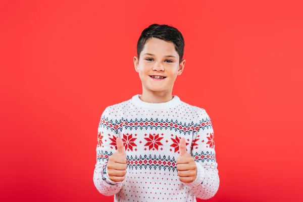 Front view of smiling child in sweater showing thumbs up isolated on red — Stock Photo