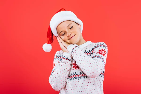 Kid in sweater and santa hat sleeping isolated on red — Stock Photo