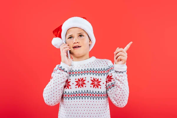 Displeased child in santa hat talking on smartphone isolated on red — Stock Photo