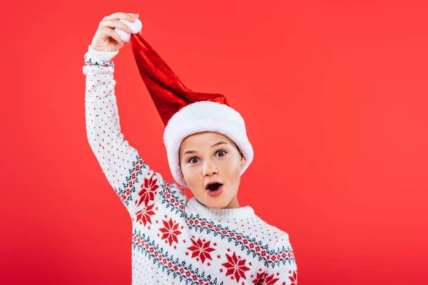 Front view of cheerful kid in sweater and santa hat isolated on red — Stock Photo