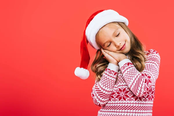 Enfant en pull et santa chapeau dormir isolé sur rouge — Photo de stock