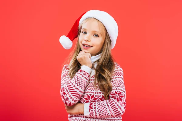 Lindo niño sonriente en suéter y sombrero de santa aislado en rojo - foto de stock