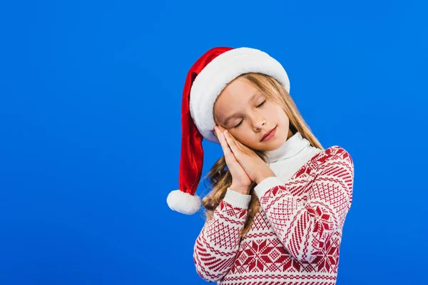 Cute kid in santa hat and sweater sleeping isolated on blue — Stock Photo