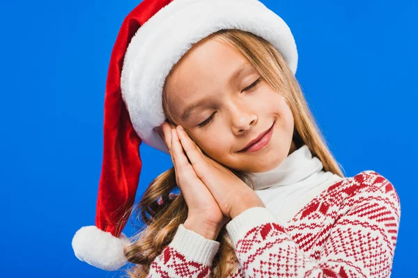 Cute kid in santa hat and sweater sleeping isolated on blue — Stock Photo