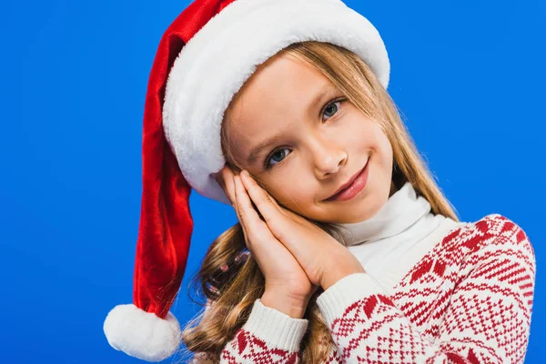 Cute smiling kid in sweater and santa hat isolated on blue — Stock Photo