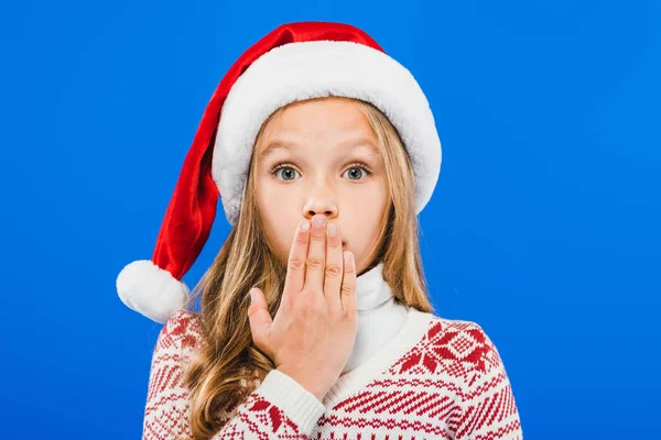 Вид спереду здивованої дитини в капелюсі Санта ізольовано на синьому — стокове фото