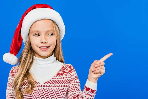 Frontansicht eines lächelnden Kindes mit Weihnachtsmütze, das mit dem Finger auf blau zeigt — Stockfoto