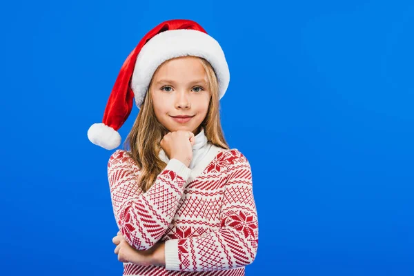 Vista frontale del bambino sorridente in maglione e cappello di Babbo Natale isolato sul blu — Foto stock