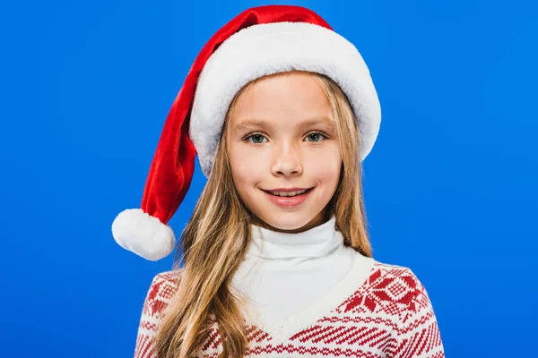 Vista frontale del bambino sorridente in cappello di Babbo Natale e maglione isolato su blu — Foto stock
