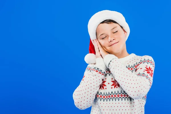 Niño en sombrero de santa y suéter durmiendo aislado en azul - foto de stock